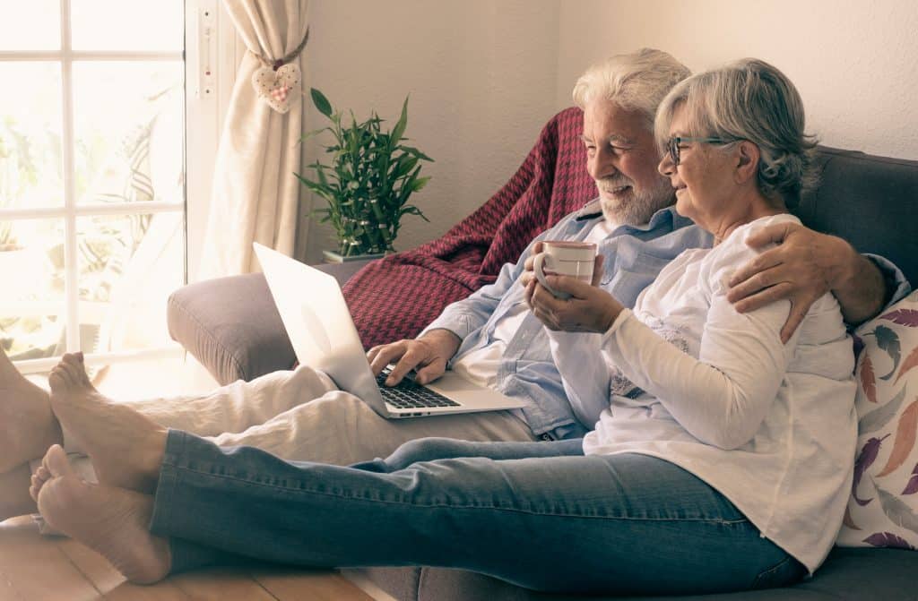 Relaxed senior couple lying on sofa at home using laptop to look at equity release companies.